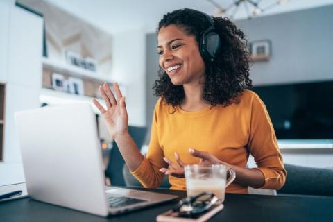 a woman wearing a headset smiling and waving at laptop screen